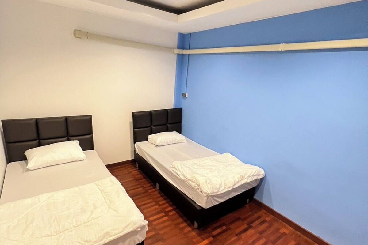 A room with two beds, wooden flooring, and a blue accent wall.