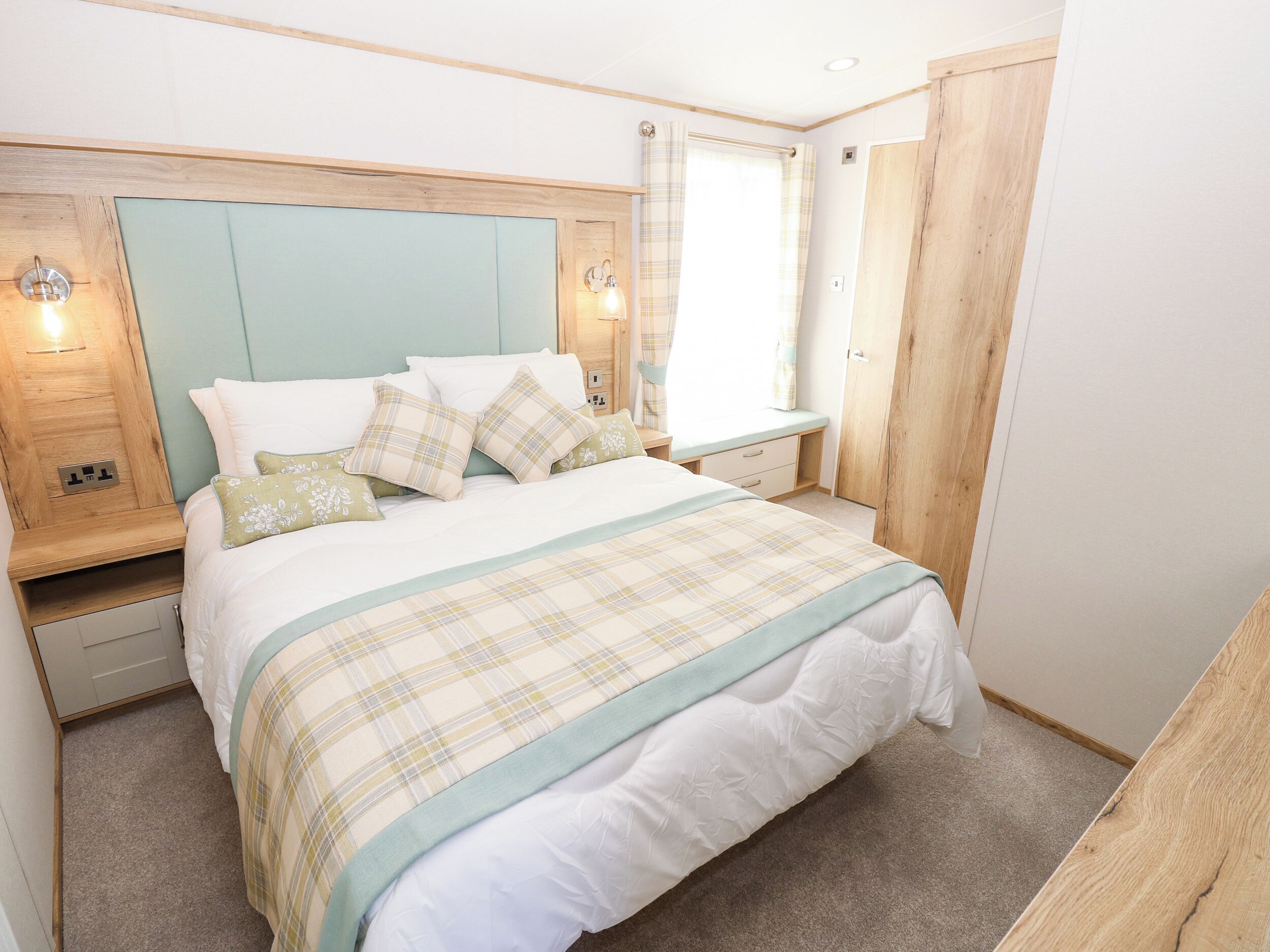 A neatly arranged bedroom with a bed, bedside tables, a nightstand, and a window with curtains.