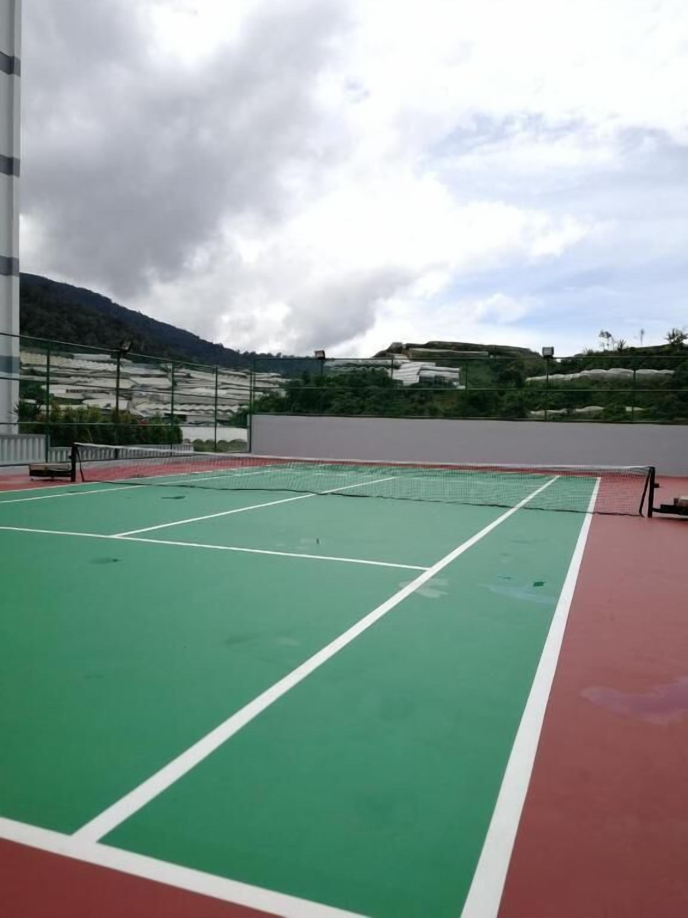 An outdoor tennis court with a green playing surface and a red surrounding area.
