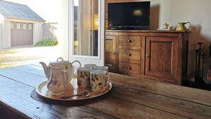 A wooden table with a tray of teapots and cups, a television on a wooden cabinet, and a window with a view of a house and fence.