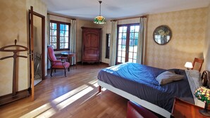 A bedroom with a bed, a chair, a desk, a wardrobe, and a hanging light fixture.