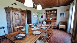 A wooden dining table with chairs, a vase with flowers, and a shelf with dishes.