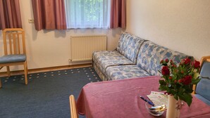 A cozy room with a wooden chair, a patterned sofa, a table with a red tablecloth, a vase with flowers, and a window with curtains. - Sonnenschein B by Interhome (Spiss-Samnaun)