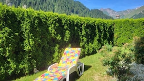 A lounge chair with a colorful floral pattern in a grassy area with a backdrop of a neatly trimmed hedge and a mountainous landscape. - Sonnenschein B by Interhome (Spiss-Samnaun)
