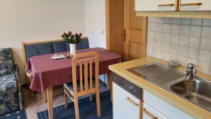 A compact kitchen with a sink, wooden cabinets, a dining table with a red tablecloth, and a chair. - Sonnenschein B by Interhome (Spiss-Samnaun)