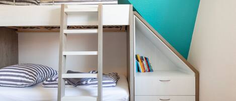A bunk bed with a ladder, a small desk with drawers, and a bookshelf under a slanted ceiling.