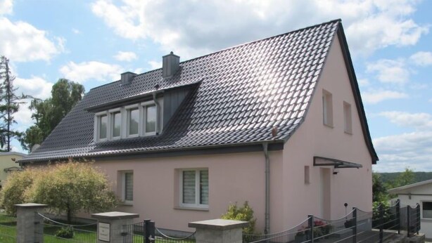 A two-story house with a tiled roof, a front porch, and a fenced yard.