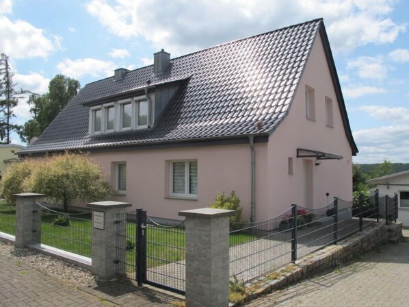 Une maison à deux étages, avec un toit en tuiles, un porche à l’avant et une cour clôturée.