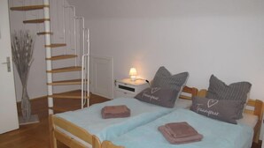 A bedroom with a wooden bed, two pillows, a bedside table with a lamp, and a staircase.