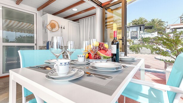 Een terras met een tafel voor vier personen, compleet met borden, glazen en een fles wijn.