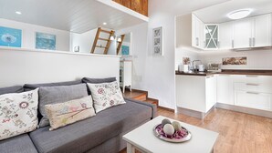 Een moderne woonkamer met een grijze bank, een witte salontafel en een keukenhoek met witte kastjes en een houten aanrecht.