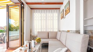 Een moderne woonkamer met een beige bank, een klein tafeltje met een dienblad en een raam met dunne gordijnen.