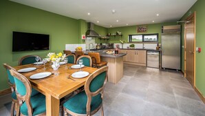 Una cocina moderna con paredes verdes, mesa de comedor de madera y sillas, equipada con horno empotrado y refrigerador.