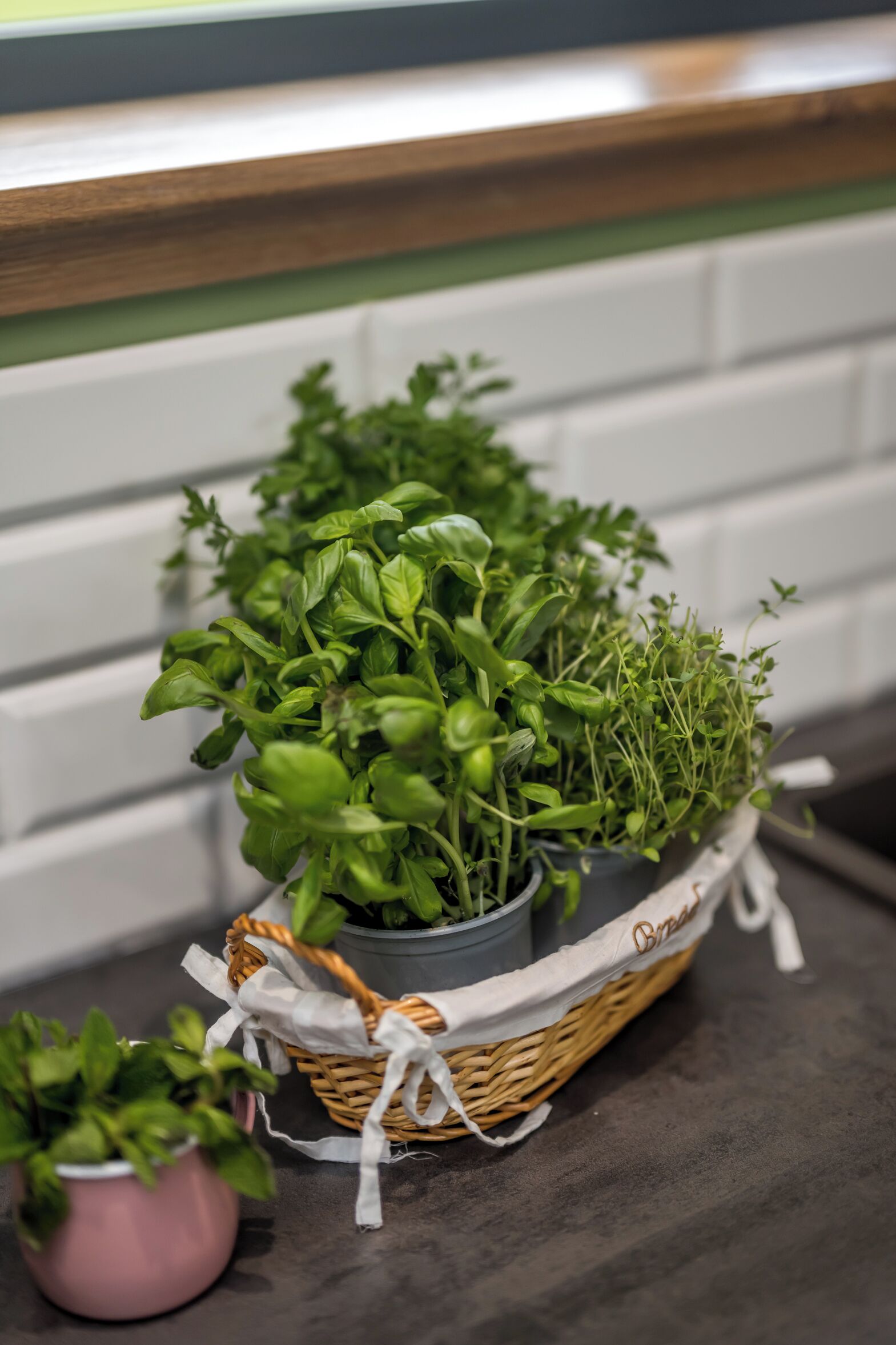 Un plan de travail de cuisine avec un panier d’herbes fraîches et une petite plante en pot.