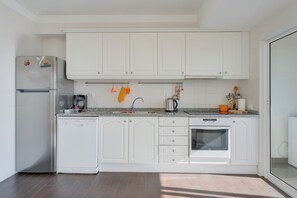 A modern kitchen with white cabinetry, a stainless steel refrigerator, a dishwasher, a coffee maker, and a toaster.
