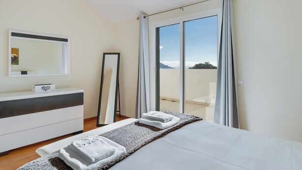 Una habitación de hotel con cama, mesita de noche, espejo y vistas al exterior.