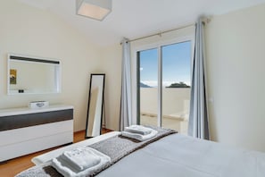 A hotel room with a bed, a bedside table, a mirror, and a view of the outdoors.