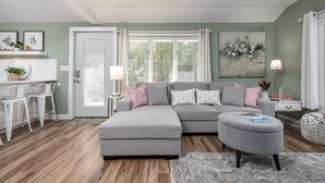 A modern living room with a grey sectional sofa, a small ottoman, a white coffee table, and a bar area with white stools. - Relax & Unwind at Anna's Place! Stylish interior, gardens + a beautiful patio.  (Harrison)