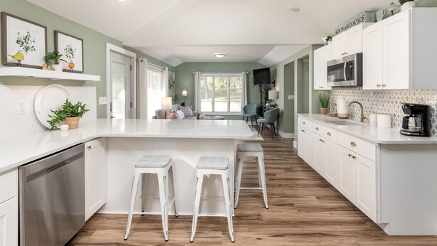A modern kitchen with white cabinetry, a central island with stools, and a dining area in the background. - Relax & Unwind at Anna's Place! Stylish interior, gardens + a beautiful patio.  (Harrison)