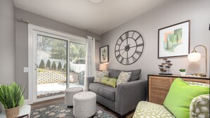 A modern living room with a grey sofa, ottoman, and green cushions, a large wall clock, and a framed abstract painting. - Relax & Unwind at Anna's Place! Stylish interior, gardens + a beautiful patio.  (Harrison)