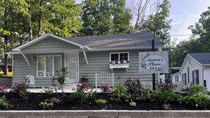 A small house with a porch, a sign reading "Anna's Place 501", and a garden with various plants and flowers. - Relax & Unwind at Anna's Place! Stylish interior, gardens + a beautiful patio.  (Harrison)
