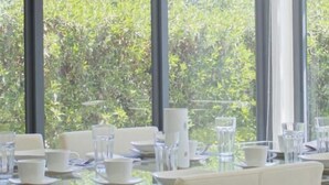 A dining area with a glass table and chairs, large windows with a view of greenery, and a modern interior design. - Joya Vacation Club (Vítor)