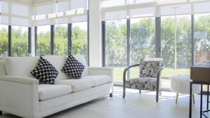 A spacious room with a white sofa and patterned armchair, large windows offering a view of greenery outside. - Joya Vacation Club (Vítor)