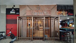 A building entrance with a metal gate, a bicycle parked to the left, and a red shutter door to the right. - Modern Studio Next to Arpoador Jc1012 Z2 (Rio de Janeiro)