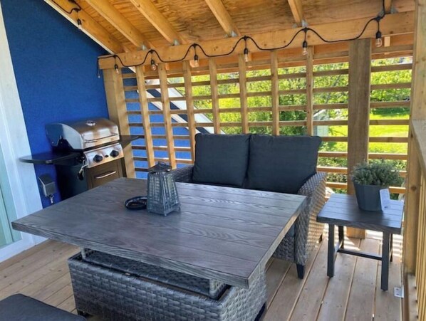 Un patio al aire libre con una mesa de madera, una parrilla y una zona de estar con cojines.