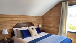 Une chambre à coucher avec une tête de lit en bois, un lit recouvert d’une couvre-lit bleue et blanche, et une table de chevet avec une lampe.