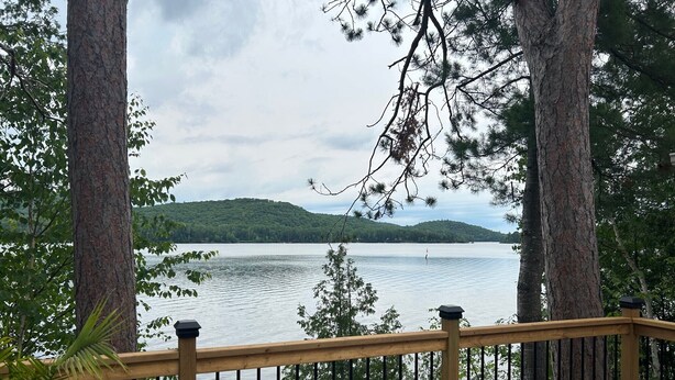 A wooden deck overlooking a calm lake with trees framing the view. - Lake House Barry's Bay (Barry's Bay)
