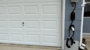 A garage door with a power outlet and a charging station mounted on the wall. - Cape Mindy HOT TUB Sleeps 8, Dog & EV Friendly, Outdoor Shower (Cape May)