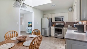 A modern kitchen with white cabinets, stainless steel appliances, and a dining area with a wooden table and chairs. - Cape Mindy HOT TUB Sleeps 8, Dog & EV Friendly, Outdoor Shower (Cape May)