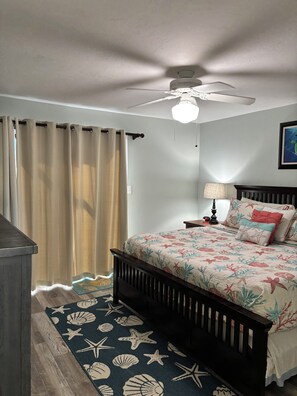 A bedroom with a bed, a ceiling fan, a nightstand, a lamp, and a rug with a sea theme.