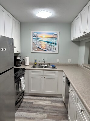 A modern kitchen with white cabinets, stainless steel appliances, a granite countertop, and a painting of a beach scene above the sink.