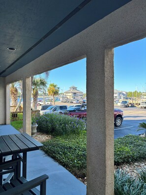 A covered outdoor area with a concrete bench, a view of a parking lot, and a building with a tower in the background.