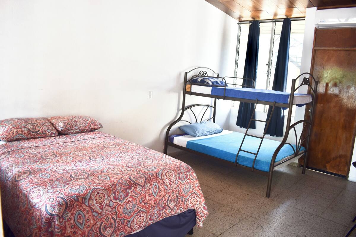 Een slaapzaal met een stapelbed, een enkel bed met beddengoed met een patroon, en een raam met gordijnen.