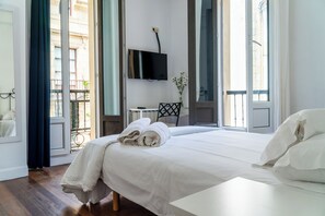 Quarto de hotel com uma cama grande, televisão na parede, uma mesinha e uma cadeira.