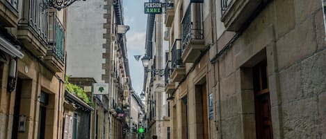 A narrow street lined with historic buildings, featuring balconies and signage for businesses like 'Pension Anne' and 'Intza'.