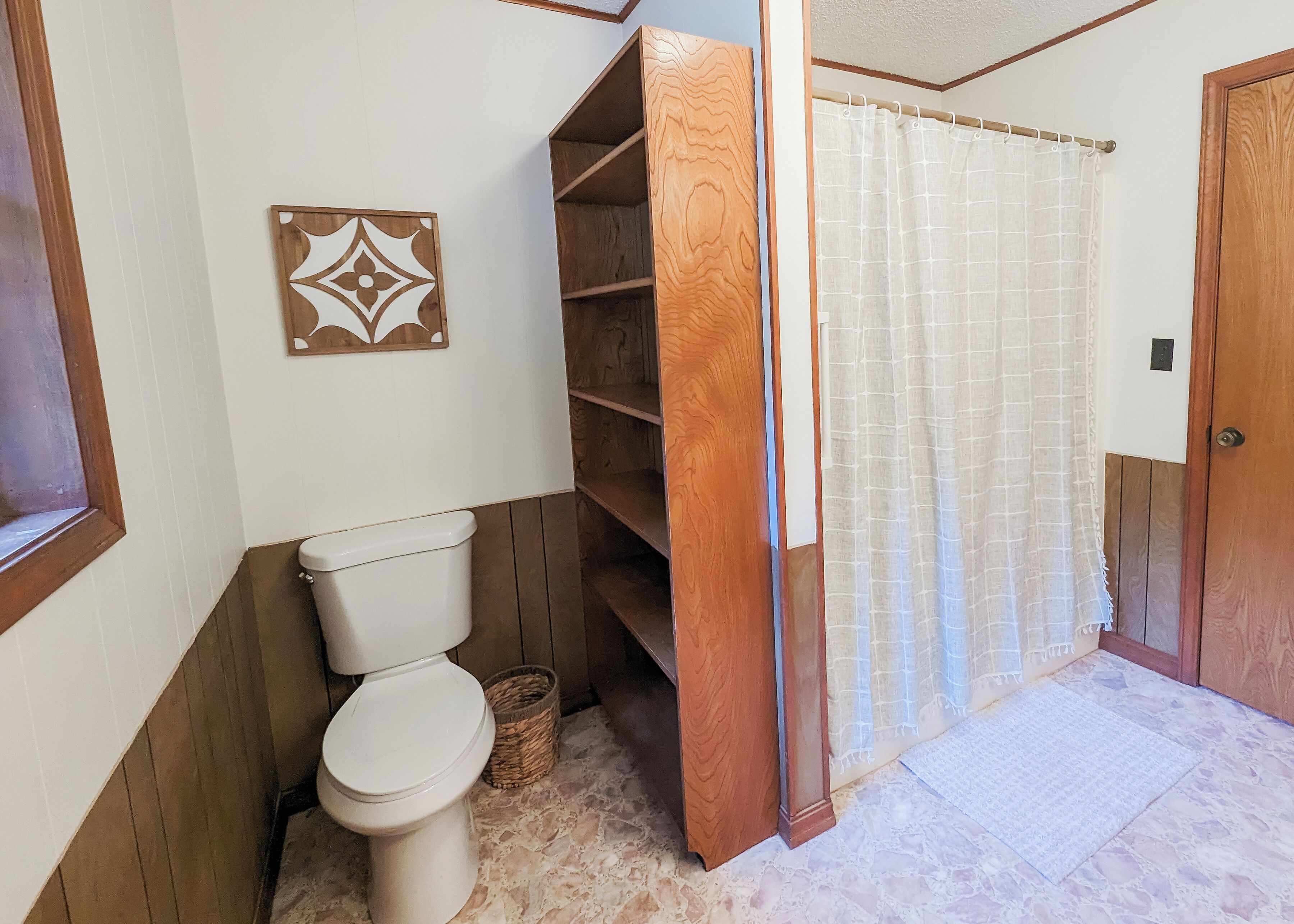 Un bany amb vàter, prestatges de fusta, una decoració de paret amb dibuixos i un teló de dutxa.