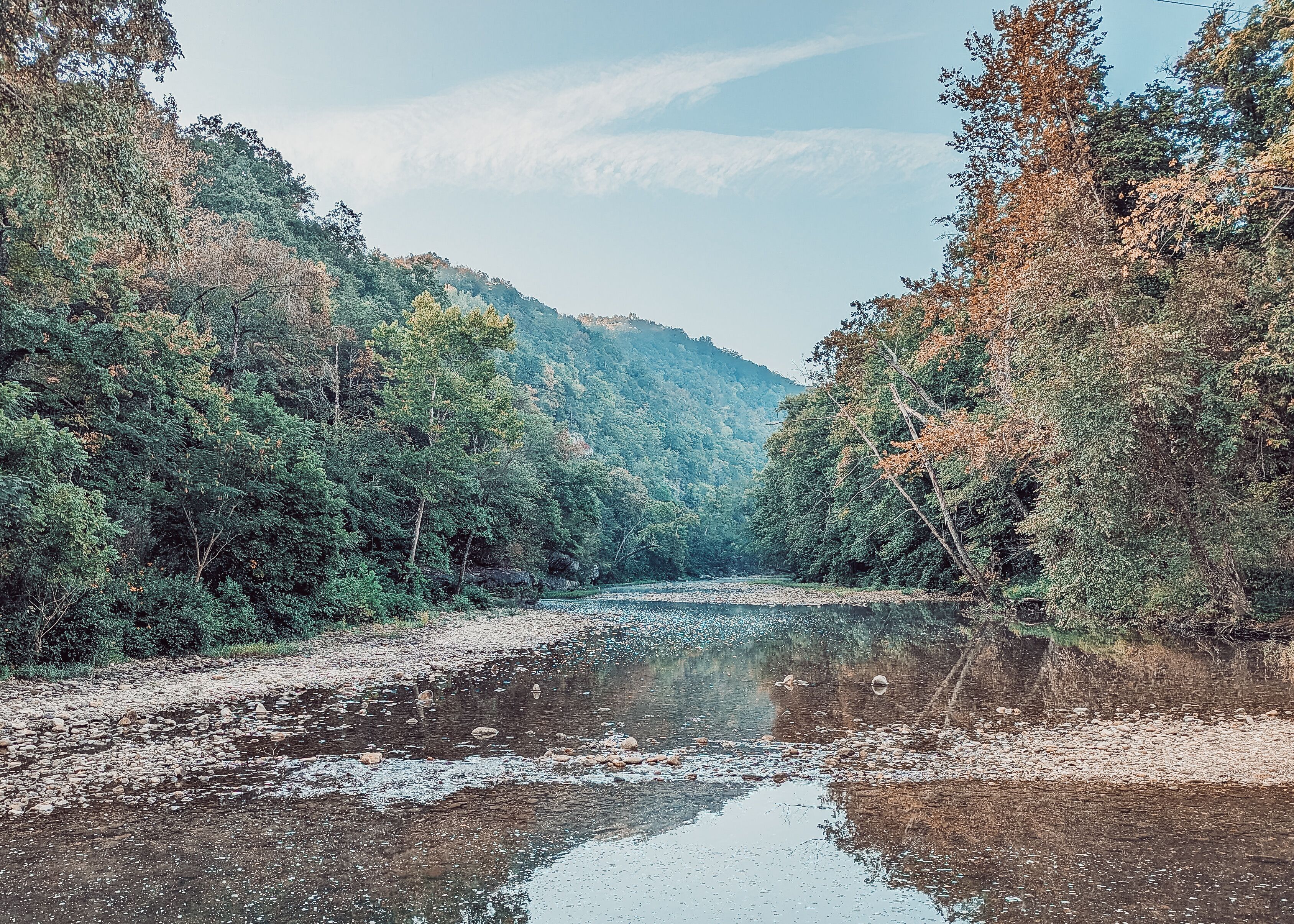 A river with a rocky bed, surrounded by dense forest and hills.