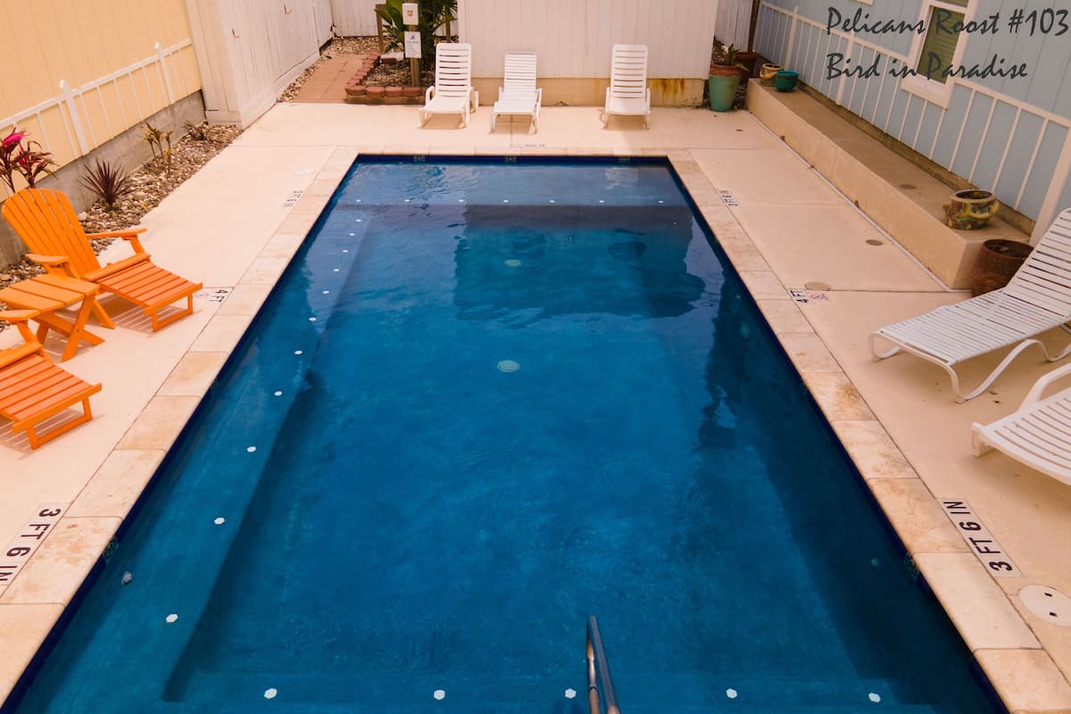 A rectangular swimming pool with a diving board, surrounded by lounge chairs and a tiled deck.