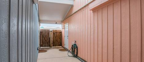 A covered outdoor corridor with a wooden gate, a hose reel, and a door.