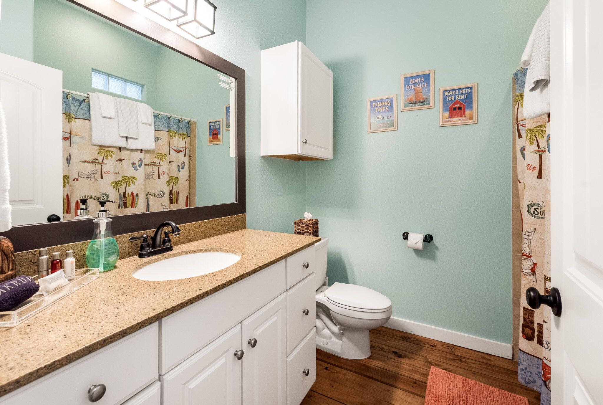 A bathroom with a sink, toilet, and a mirror. There are framed pictures on the wall and a towel rack with towels.