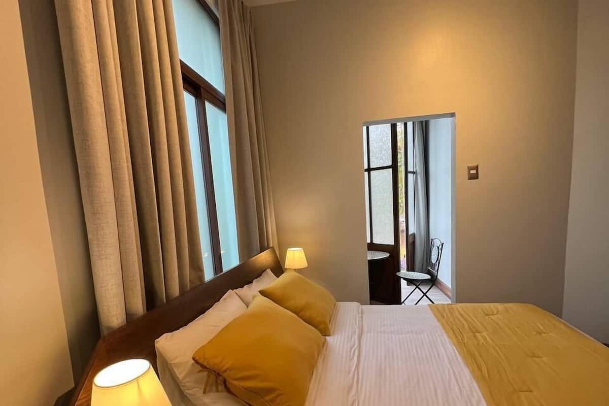 Une chambre d’hôtel avec un lit, une table de chevet, une lampe et une fenêtre avec des rideaux.