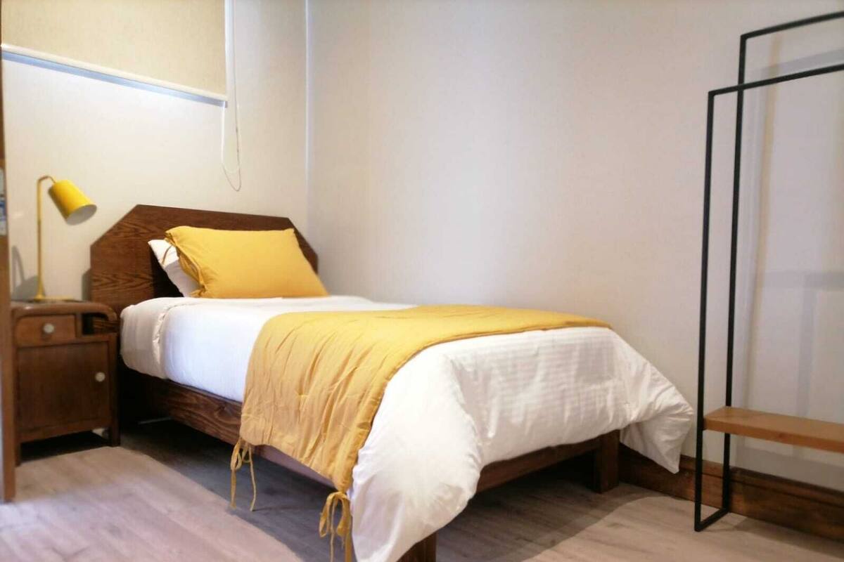Une chambre à coucher bien rangée, avec un lit, une table de chevet, une lampe et un petit banc en bois.