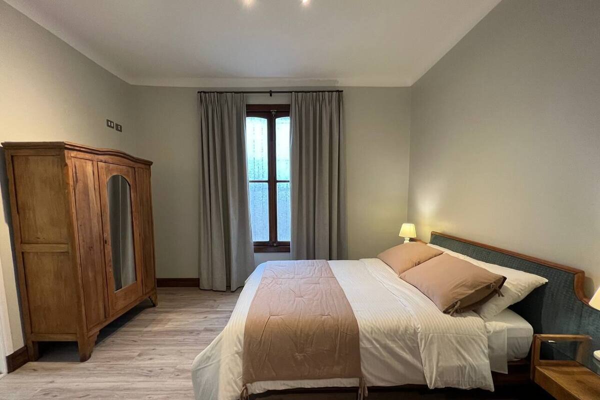 Une chambre à coucher avec un lit, une armoire en bois, une fenêtre avec des rideaux et une table de chevet avec une lampe.