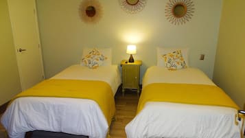 Una habitación con dos camas, cada una con cubrecama amarillo y ropa de cama blanca, una mesita de noche con lámpara, y espejos decorativos con diseño de sol en la pared.
