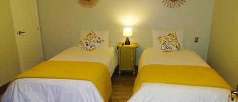 A room with two beds, each with a yellow bedspread and white bedding, a nightstand with a lamp, and decorative sunburst mirrors on the wall.
