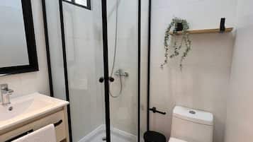 Un baño moderno con ducha de vidrio, lavamanos blanco y retrete.